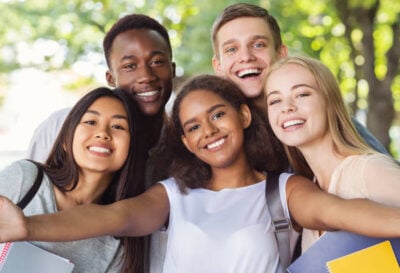 Cheerful international friends teenagers taking selfie while walking in summer park, happy memories concept